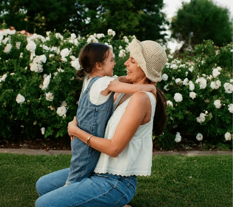 Older couple posing together outdoors, woman kissing man on the cheek while he holds a red rose